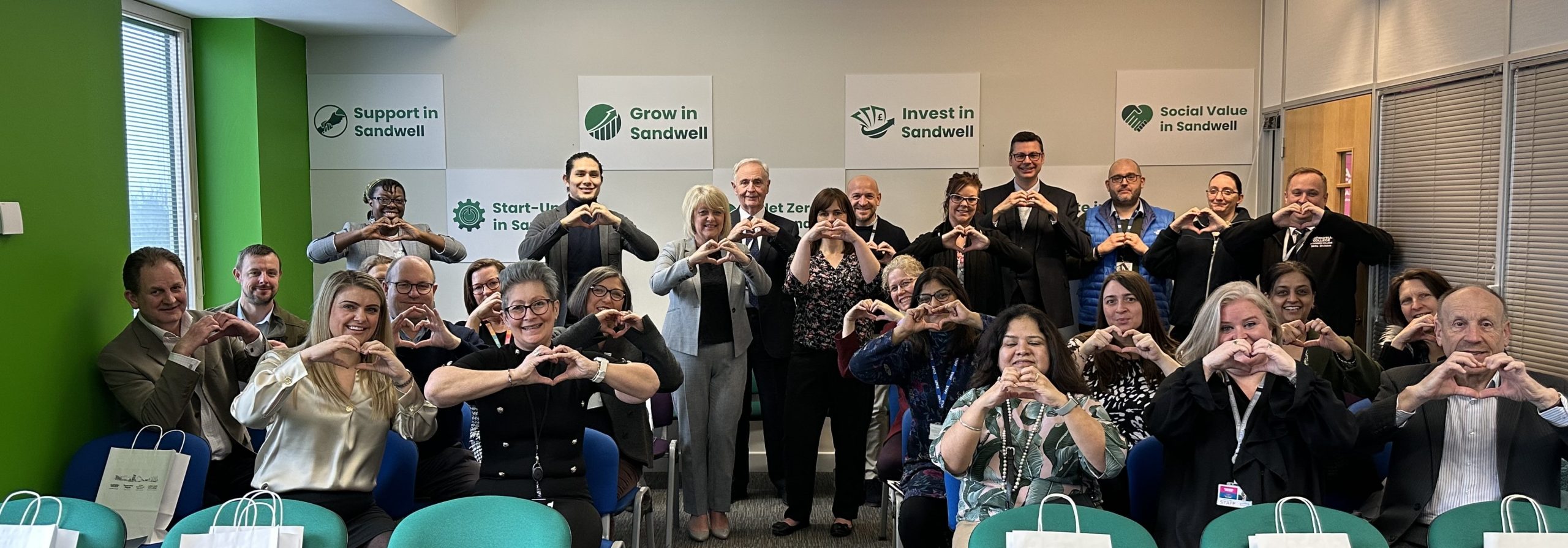 Men and women at the Sandwell Start-Up Hub making a heart symbol wit their hands for International Women's Day in 2024