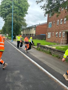 People wearing high vis PPE clothing picking up litter on a road with brown brick buildings on the right.