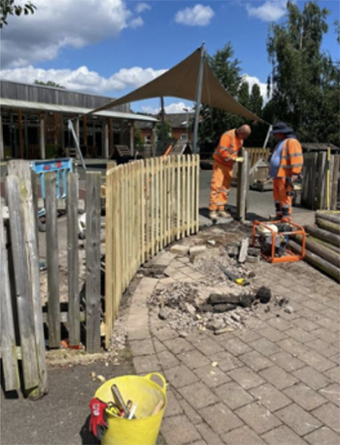 Two workers in high vis orange workwear standing in front of a wooden fence.